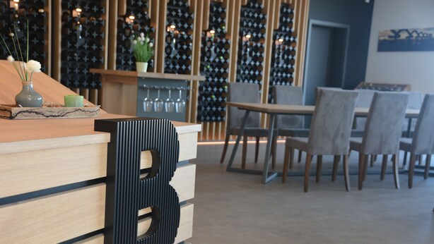 A reception area with a wooden counter, a large 'B' sign, and a wine rack in the background. - Weingut Bugner Meizelhof (Klein-Winternheim)