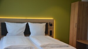 A neatly made bed with white linens in a room with green walls and a wooden headboard. - Weingut Bugner Meizelhof (Klein-Winternheim)