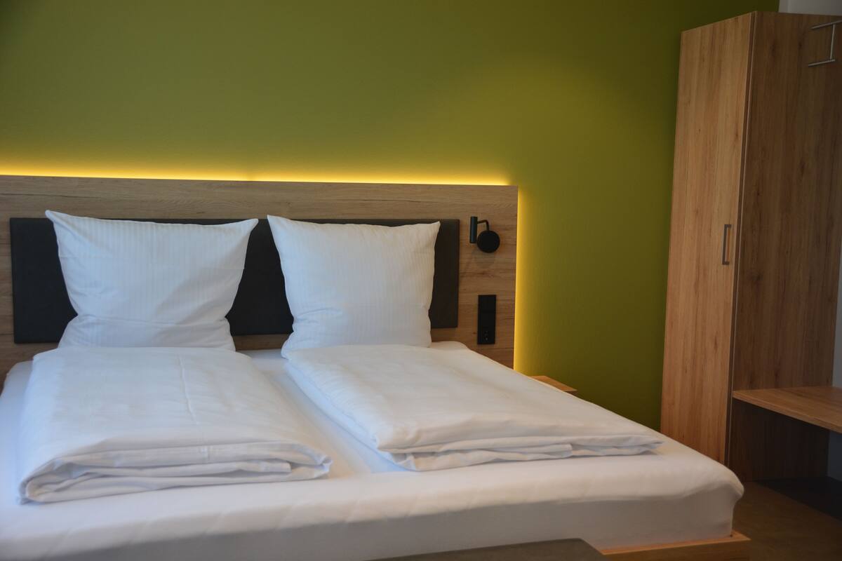A neatly made bed with white linens in a room with green walls and a wooden headboard.