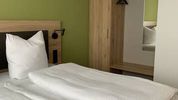 A neatly made bed with white linens in a room with green walls and a wooden wardrobe.