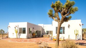 Un edificio moderno e bianco con ampie finestre, un patio con mobili da esterno e cactus in primo piano.