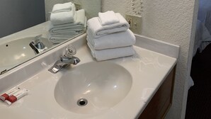 A bathroom with a sink, a mirror, a hairdryer, and a stack of towels. - Plaza inn Lordsburg (Lordsburg)