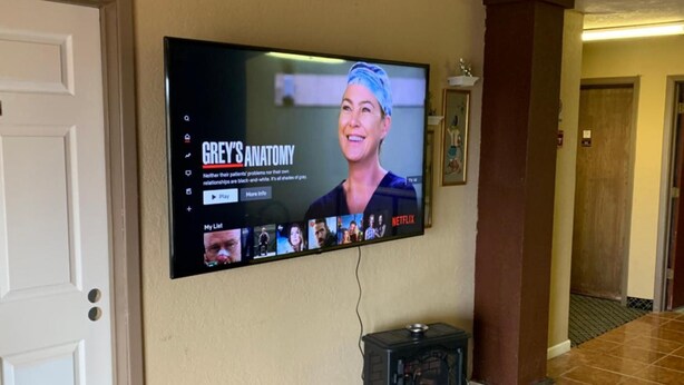 A television mounted on a wall displaying 'Grey's Anatomy' with a small black heater below it. - Plaza inn Lordsburg (Lordsburg)