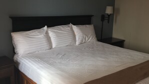 A neatly made bed with a dark headboard, a bedside lamp, and a wooden nightstand. - Plaza inn Lordsburg (Lordsburg)