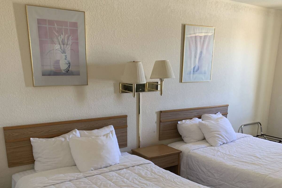 Una habitación de hotel con dos camas, una mesita de noche, lámparas de pared y cuadros enmarcados.