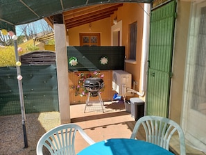 Eine Terrasse im Freien mit Tisch, Stühlen, einem Grill und einer grünen Tür.