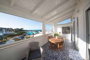 A balcony with a view of boats and a marina, a dining area with a table and chairs, and a kitchen area. - The House on the Ischia Port (Ischia)