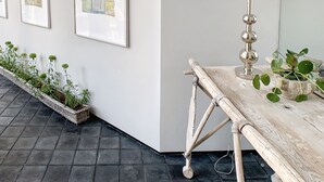 A modern interior with a white wall, framed artwork, a lamp, a wooden bench, and a planter with green plants.