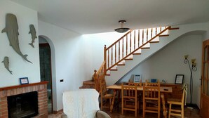 Ein Wohnzimmer mit Kamin, einem Essbereich mit Holzmöbeln, einer Treppe und einer Wand mit Hai-Dekorationen.