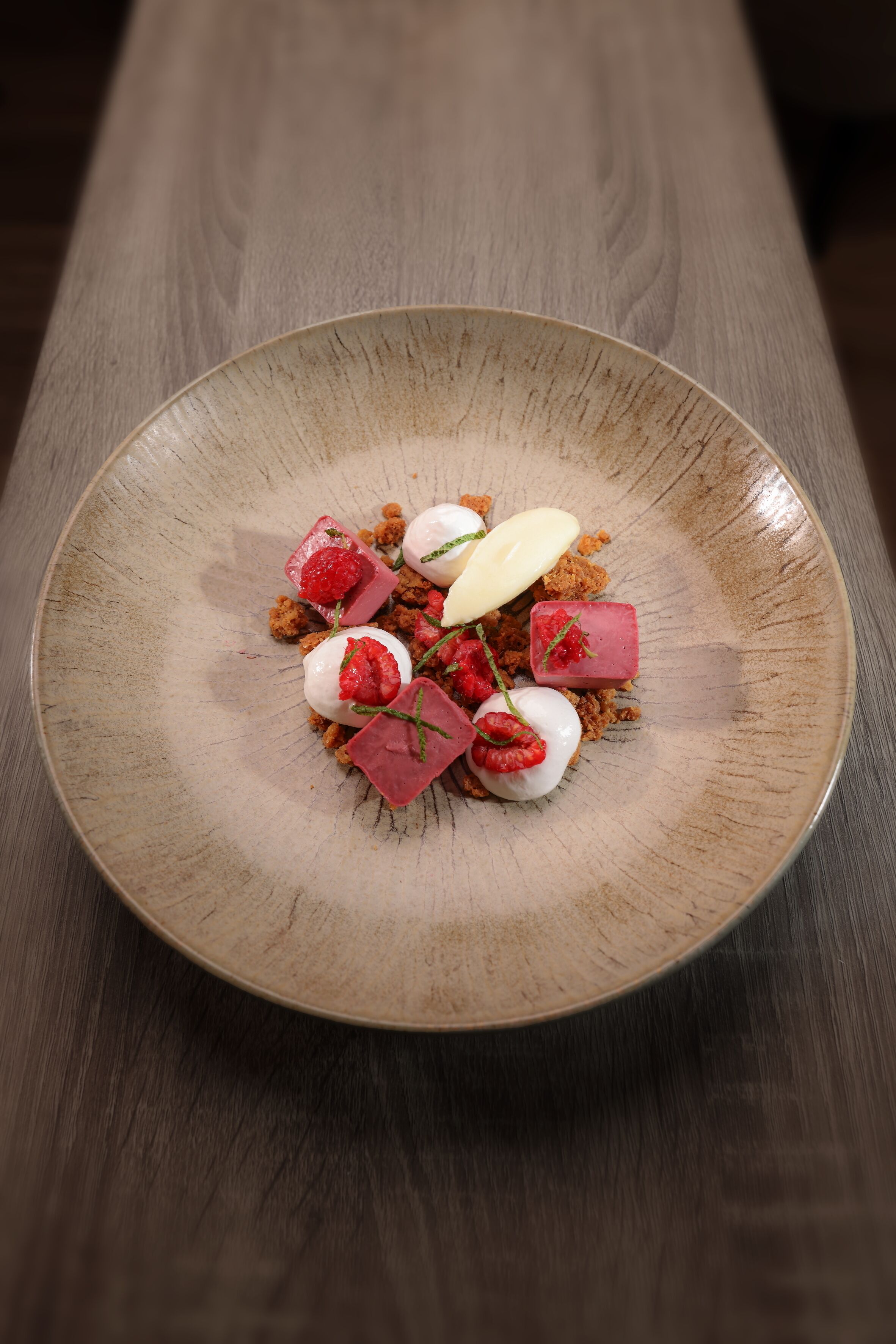 Ein Dessertteller mit Erdbeeren, Himbeeren und Würfeln auf einem Holztisch.