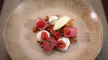 Ein Dessertteller mit Erdbeeren, Himbeeren und Würfeln auf einem Holztisch.