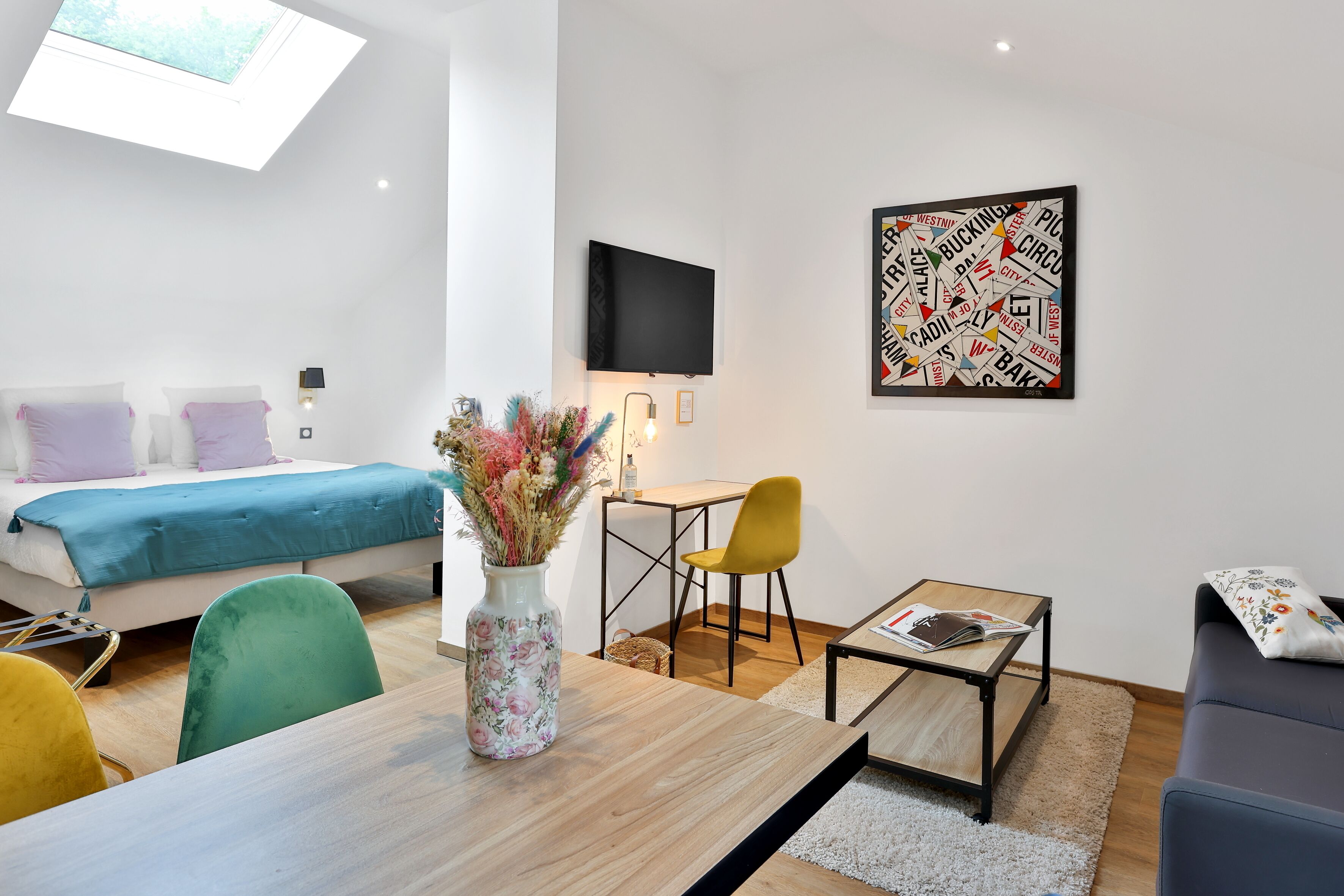 Habitació d'hotel moderna amb un llit, escriptori, cadira, taula petita, televisió i una decoració mural.