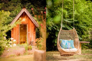 A wooden cabin with a door and a swing chair in a garden.
