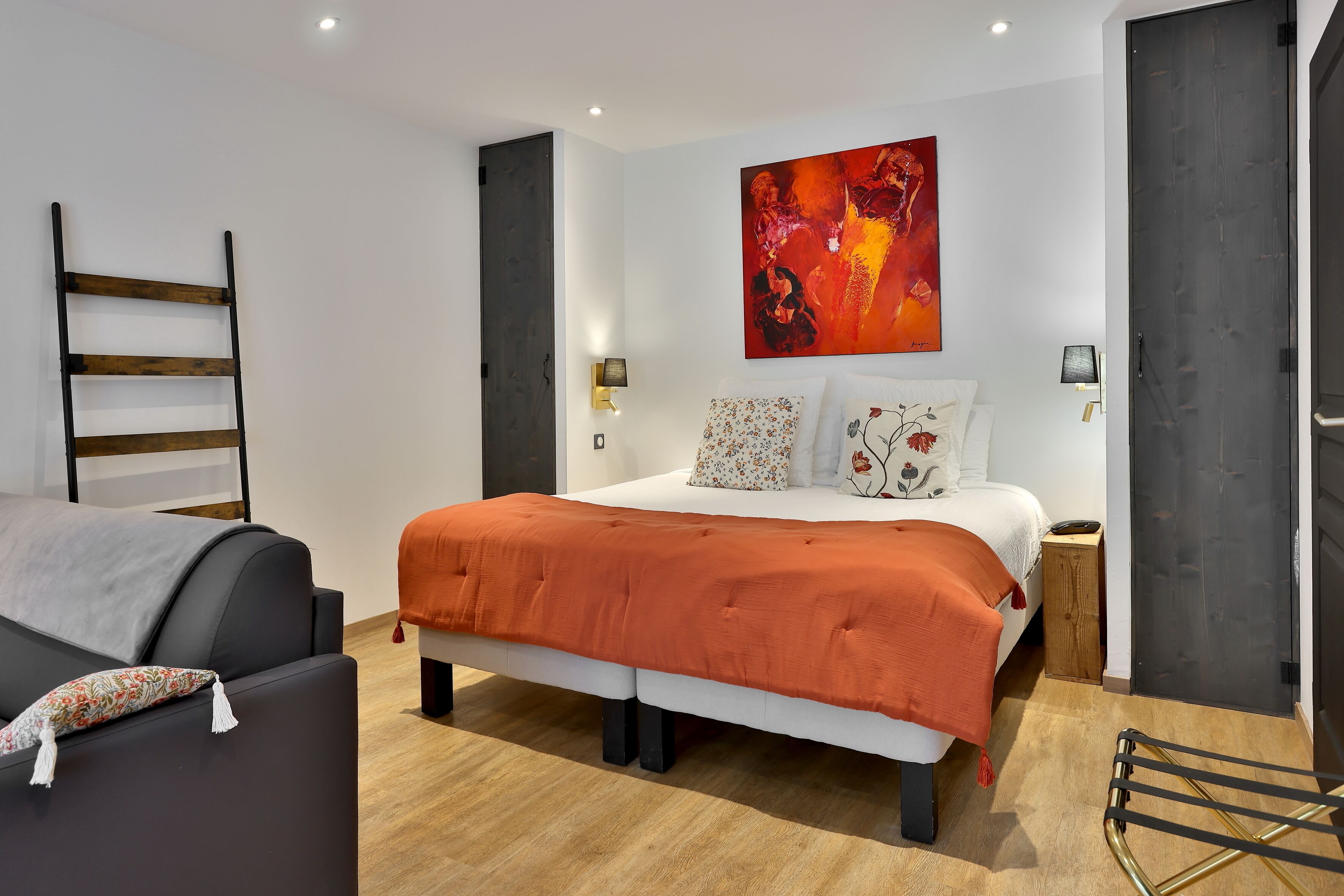 Une chambre à coucher moderne avec un grand lit, une échelle en bois, une petite table et une œuvre d’art accrochée au mur.