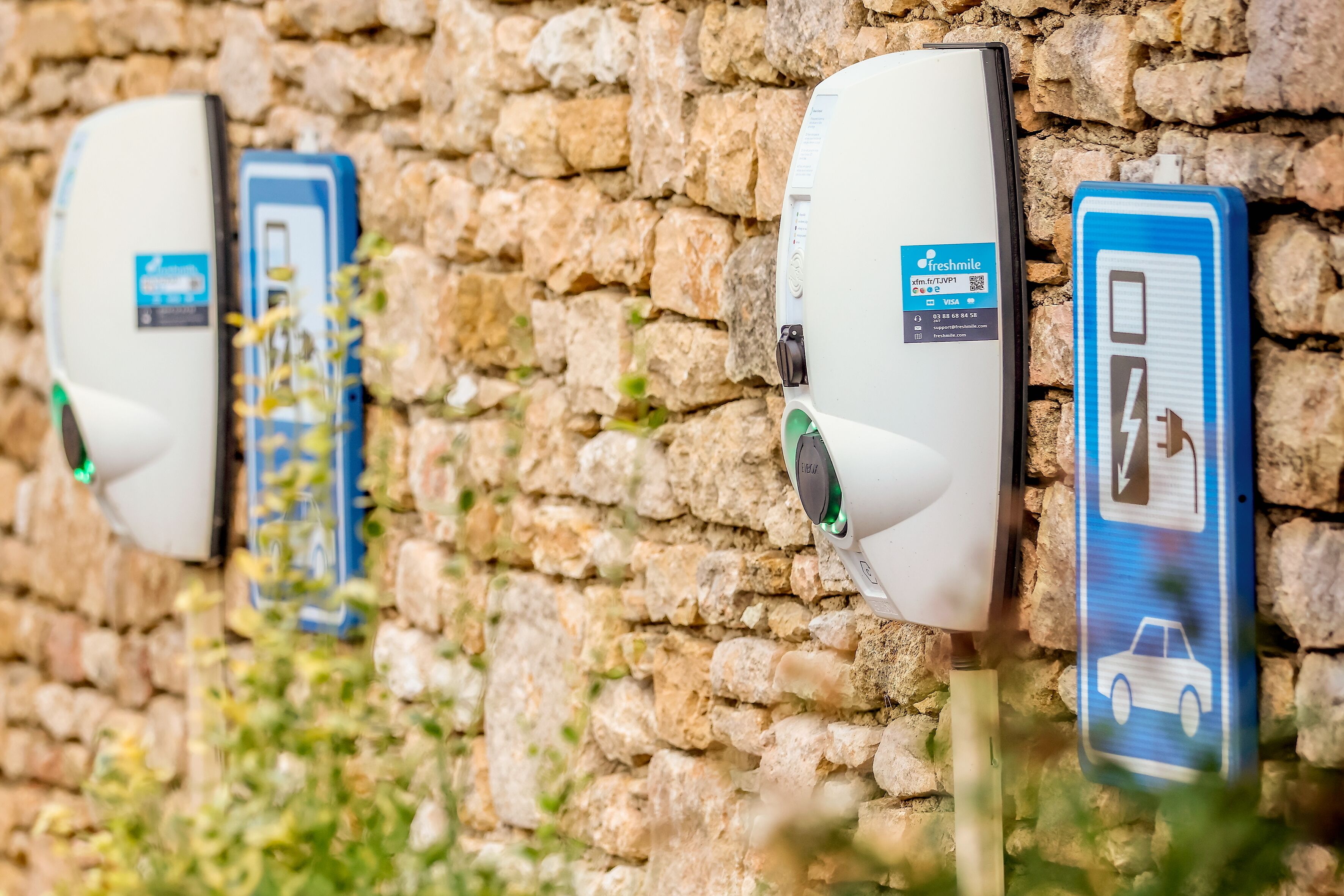 Estaciones de carga para vehículos eléctricos fijadas a un muro de piedra.