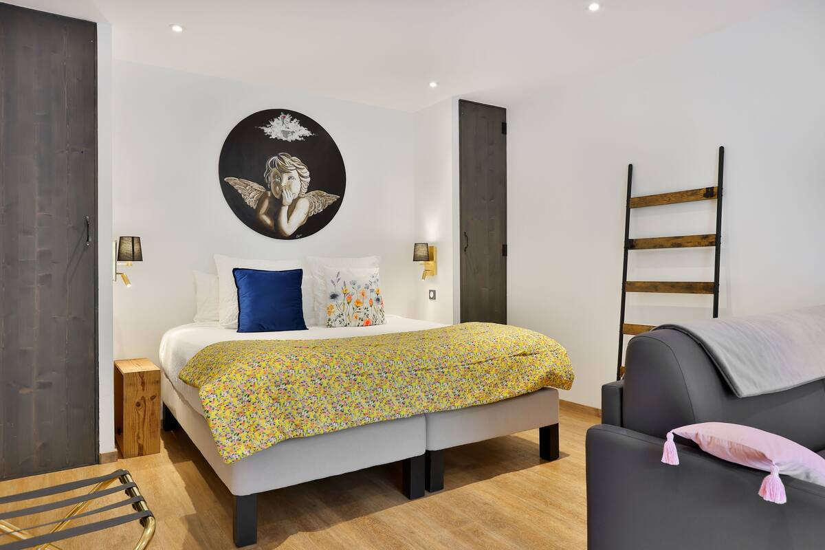 Un dormitorio moderno con una cama, un sofá, una escalera y una obra de arte en la pared.