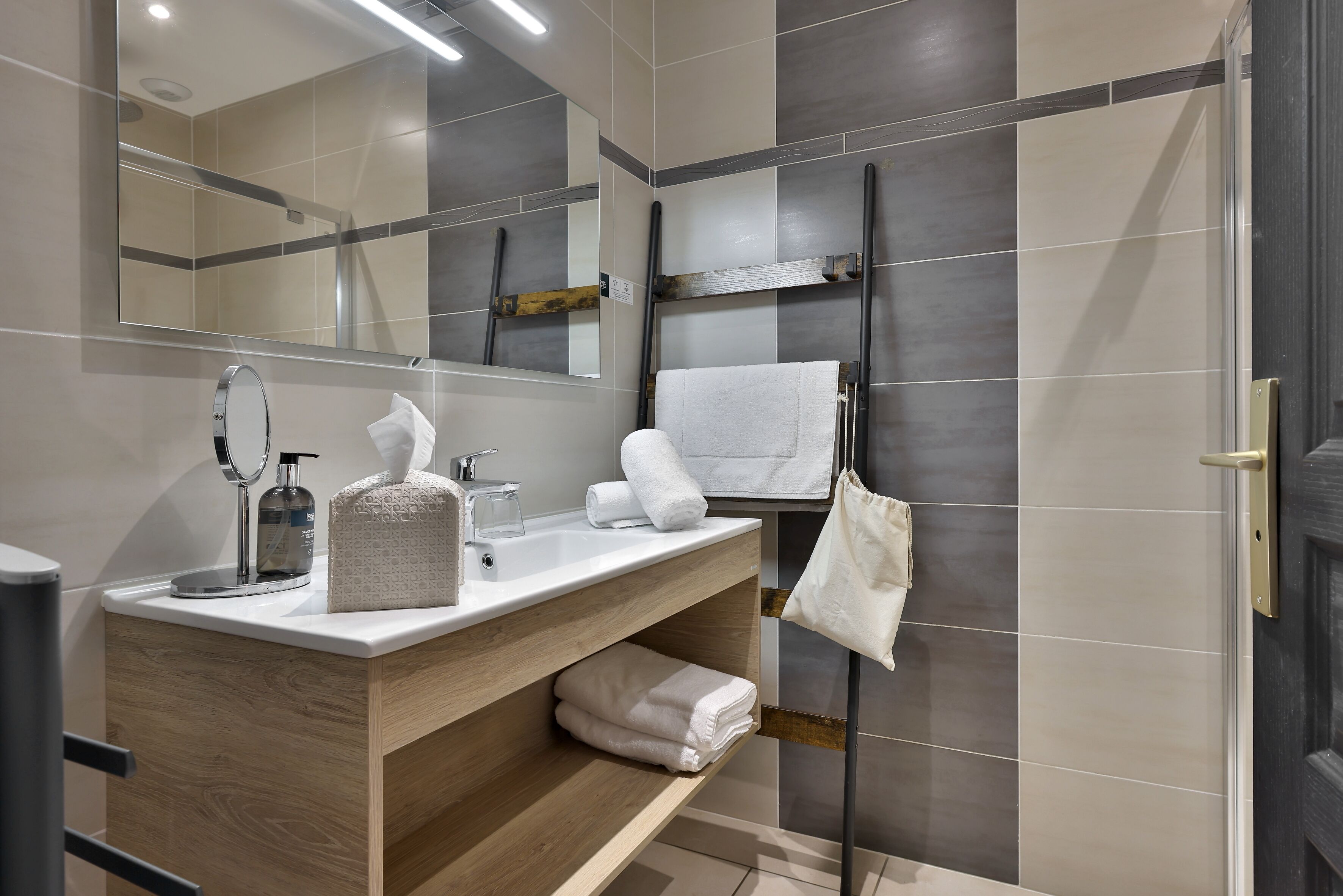 A modern bathroom with a wooden vanity, a large mirror, a towel rack, and a shower area.