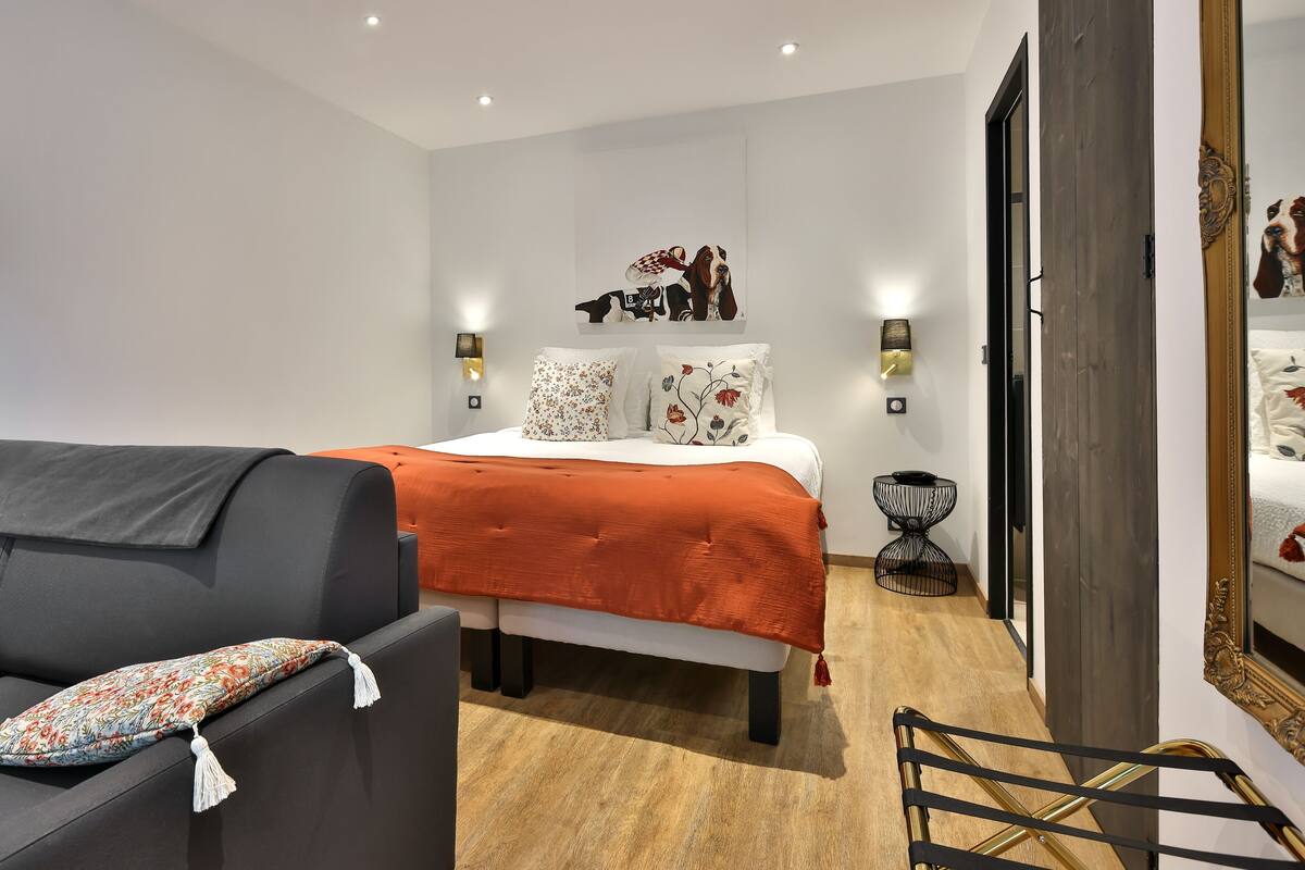 Un dormitorio moderno con cama, sofá, espejo y una mesita de noche.