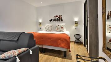Un dormitorio moderno con cama, sofá, espejo y una mesita de noche.