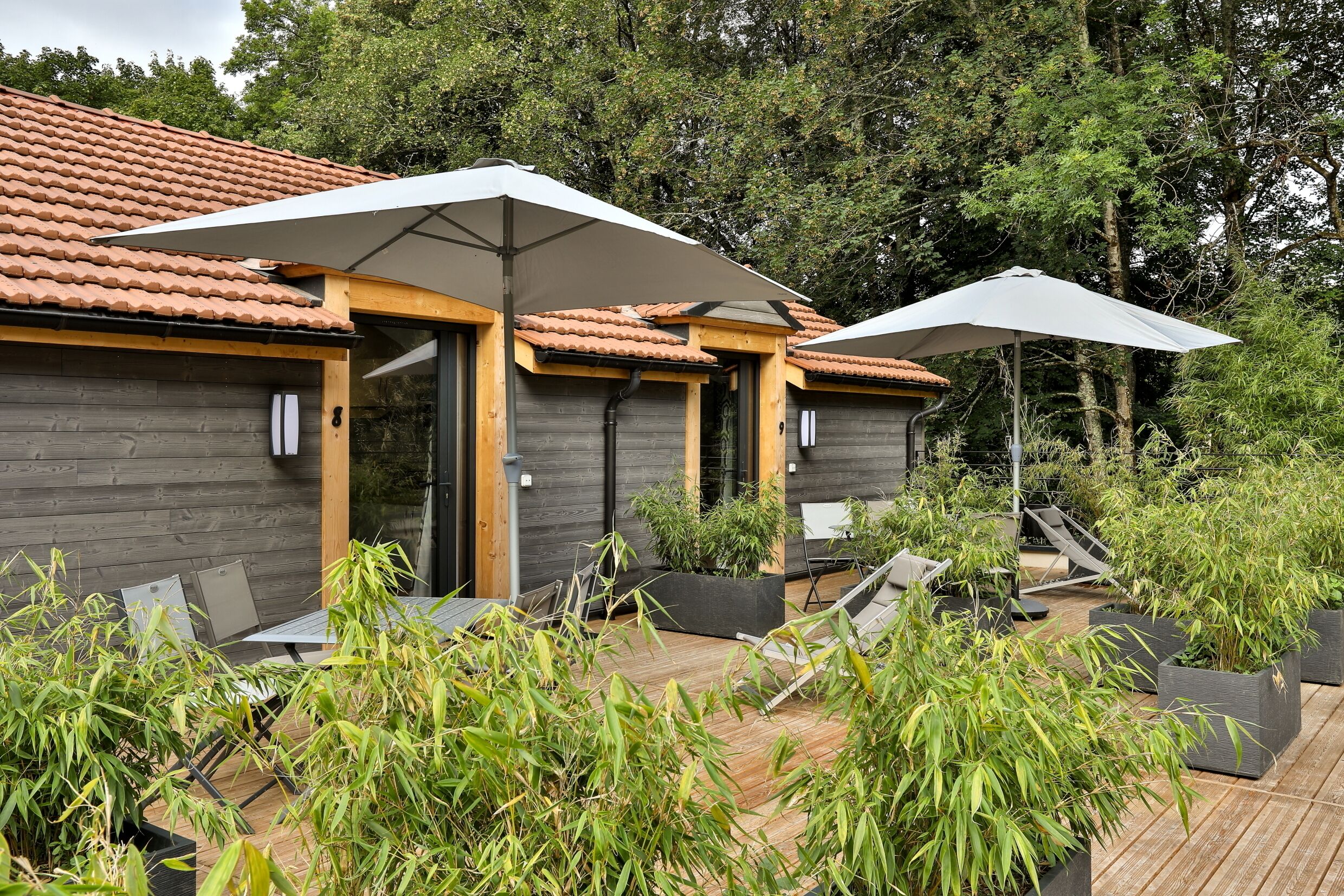 Un bâtiment moderne avec un toit en tuiles, des murs en bois et un espace extérieur aménagé avec des tables et des parasols.