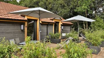 Un bâtiment moderne avec un toit en tuiles, des murs en bois et un espace extérieur aménagé avec des tables et des parasols.
