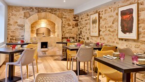 A dining area with stone walls, a brick oven, and wicker chairs. - L'Atelier d'Epicure - Logis (Castels et Bézenac)