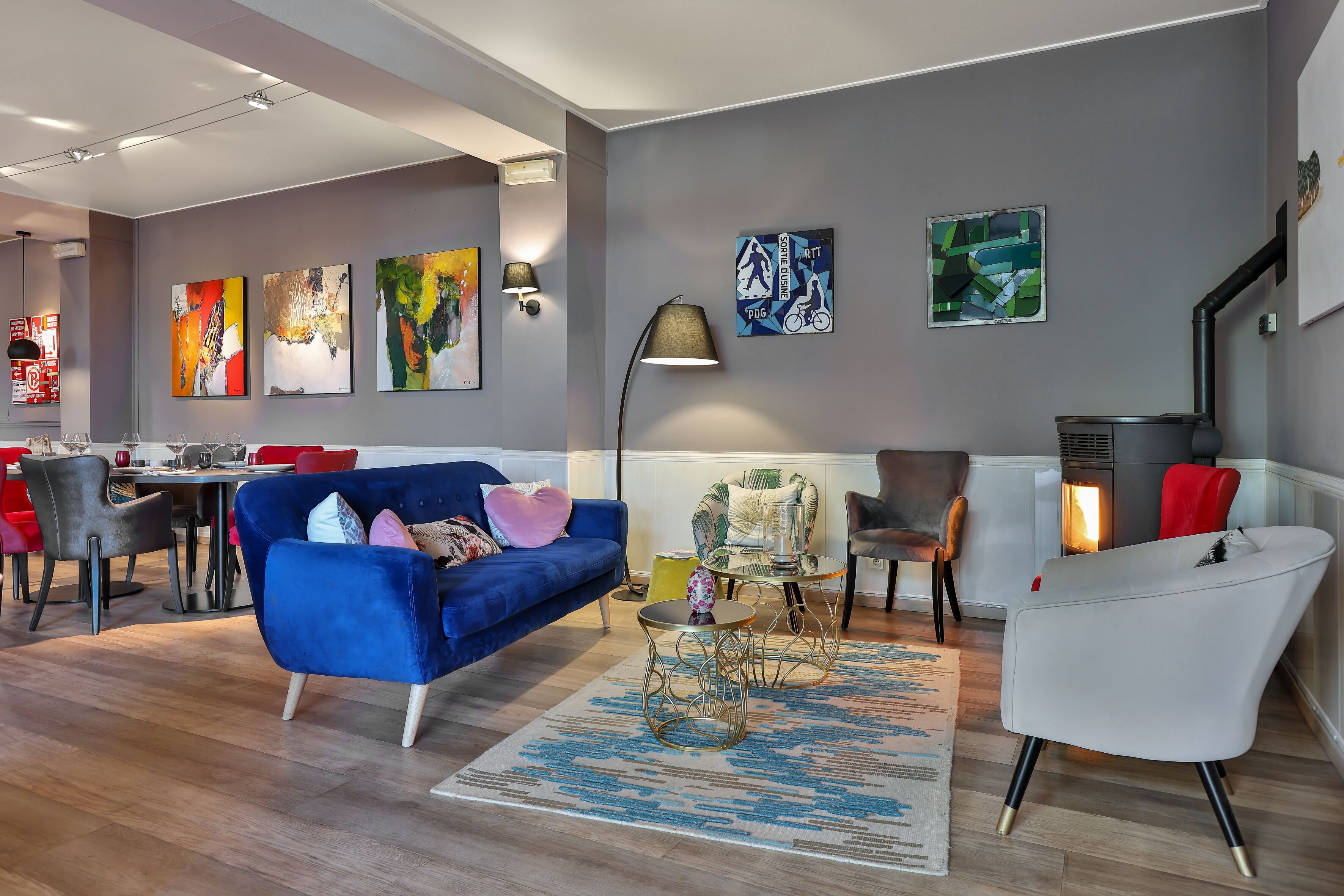 A modern living room with a blue sofa, a white armchair, and a dining area with red chairs.