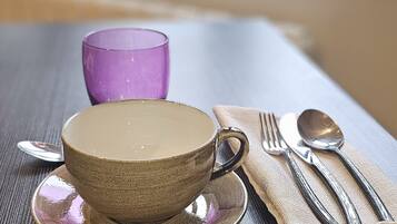 Une table avec une tasse et une soucoupe en céramique, un verre violet et une serviette avec des couverts.