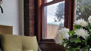 Een gezellige zithoek met een rieten bank, een groene mok met dessin, een kaars en een vaas met witte bloemen.