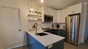 Een moderne keuken met witte kastjes, een roestvrijstalen koelkast, een magnetron en een spoelbak met een moderne kraan.