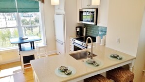 A modern kitchen with a central island, a built-in oven, and a microwave. There are three woven stools under the island. - Ocean Views!102 West Terminal Blvd Unit #15 Atlantic Beach, NC (Atlantic Beach)
