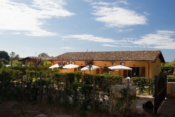 A building with a tiled roof, outdoor seating with umbrellas, and a fenced garden area.