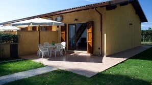 A yellow building with a tiled patio, white chairs, and umbrellas. - villa 1 with garden in the green a few meters from the beach (Sabaudia)