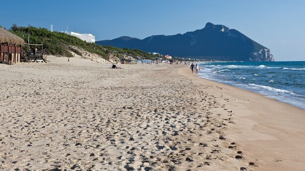 A beach with a mountain in the background, sandy terrain, and a few buildings on the left. - villa 1 with garden in the green a few meters from the beach (Sabaudia)
