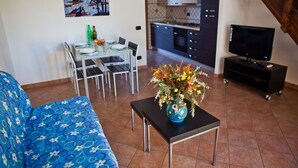 A living room with a sofa, a dining table with chairs, a TV on a stand, and a kitchen in the background. - villa 1 with garden in the green a few meters from the beach (Sabaudia)