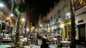 A bustling outdoor dining area with tables and chairs, surrounded by buildings with balconies and potted plants. - Apartamento Cadiz de Cine (Cádiz)