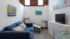 En stue med en blå sofa, et lille bord, et fjernsyn og billedkunst på væggene.
