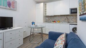 En kompakt bolig med tekøkken, sofa, TV og vaskemaskine.