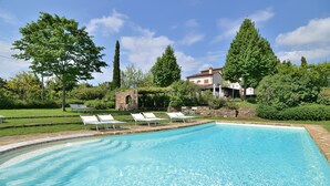 A swimming pool with lounge chairs, surrounded by greenery and a stone structure.