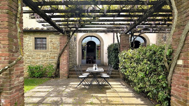 A stone patio with a table and chairs under a pergola.