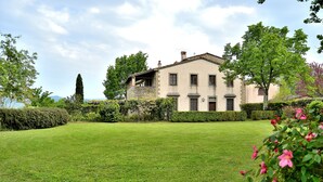 A large, two-story house with a well-maintained lawn and a variety of trees and shrubs.