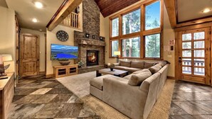 A cozy living room with a stone fireplace, a large window, and a television. - Hot Tub, Game Room, Near Lake, Walk to Trails (South Lake Tahoe)