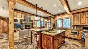 A spacious kitchen with a large island, wooden cabinets, and a stone fireplace. - Hot Tub, Game Room, Near Lake, Walk to Trails (South Lake Tahoe)