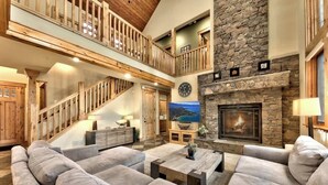 A spacious living area with a stone fireplace, a large couch, and a wooden staircase. - Hot Tub, Game Room, Near Lake, Walk to Trails (South Lake Tahoe)