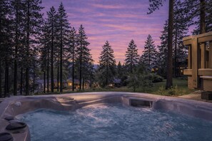 A hot tub surrounded by tall trees and a house in the background.