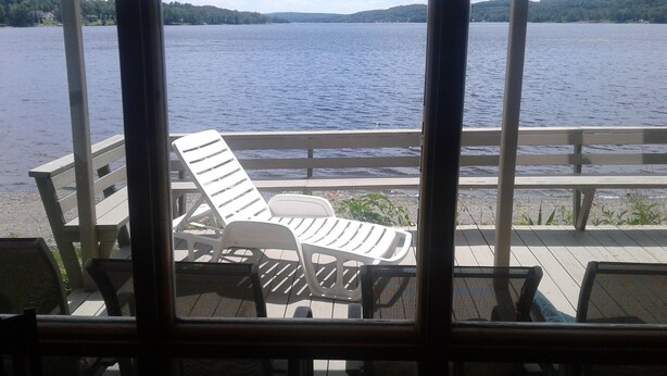 A deck with a view of a lake, featuring white lounge chairs and a wooden railing. - Lake front Rental!!!  (eagle lake)