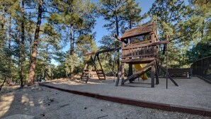 A playground with wooden climbing structures and a slide, surrounded by trees. - Close to Prescott Square,2 Pools,Playground,Tennis,Pickle Ball,Trails,Wildlife (Prescott)