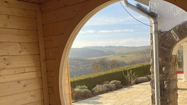 A wooden interior with a circular window revealing a stone wall and a paved outdoor area.