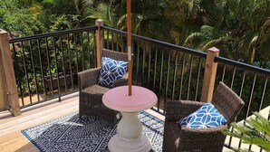 Um terraço com móveis de vime, um tapete estampado e um guarda-sol vermelho com texto.