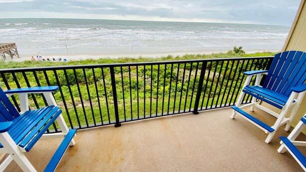 A balcony with two blue and white Adirondack chairs, a concrete floor, and a view of the ocean. - Oceanfront townhouse, 2 bedroom, 2.5 baths. (St. Augustine)